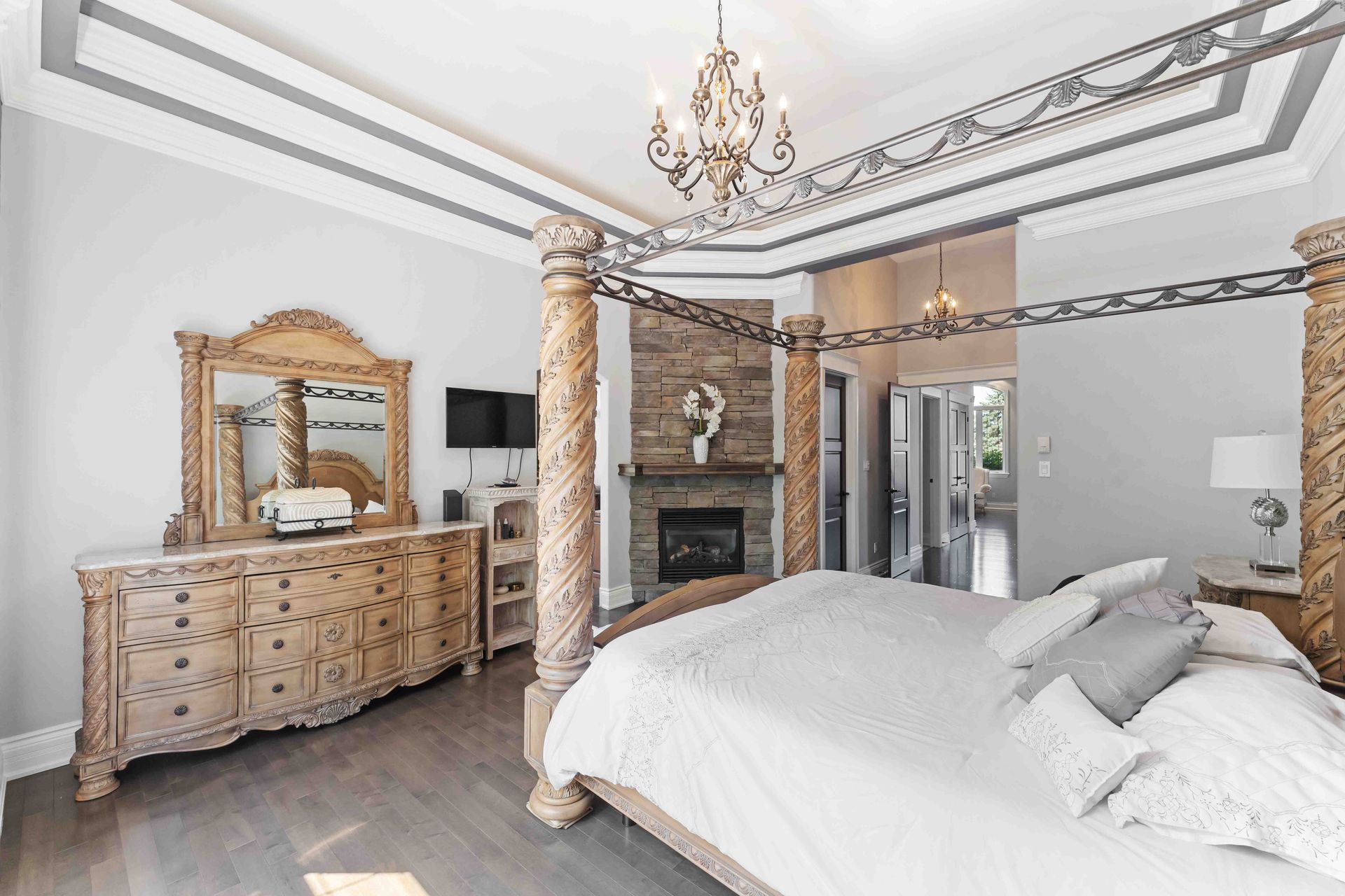 A bedroom with a four poster bed , dresser , mirror and fireplace.