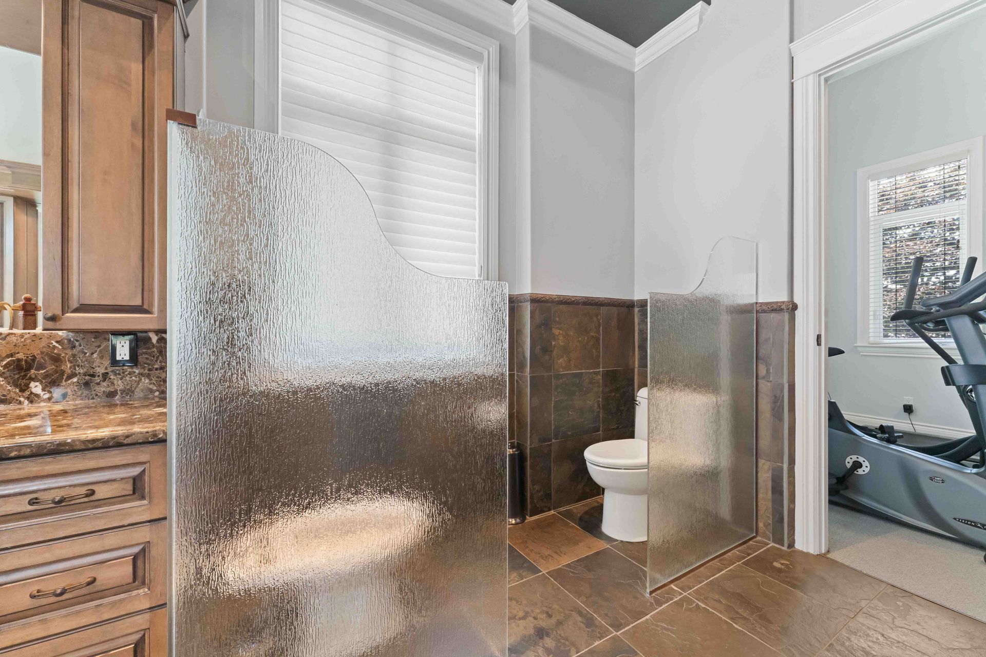 A bathroom with a walk in shower , toilet , and treadmill.