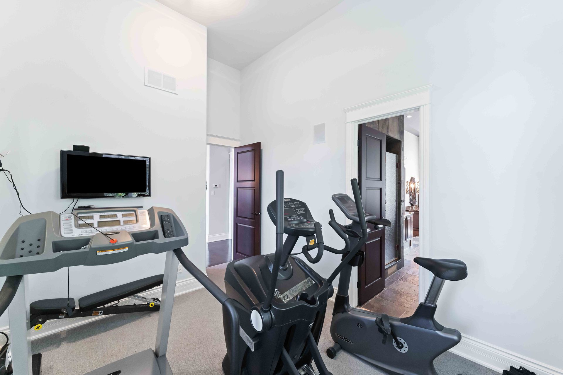 A home gym with treadmills , ellipticals , and a television.