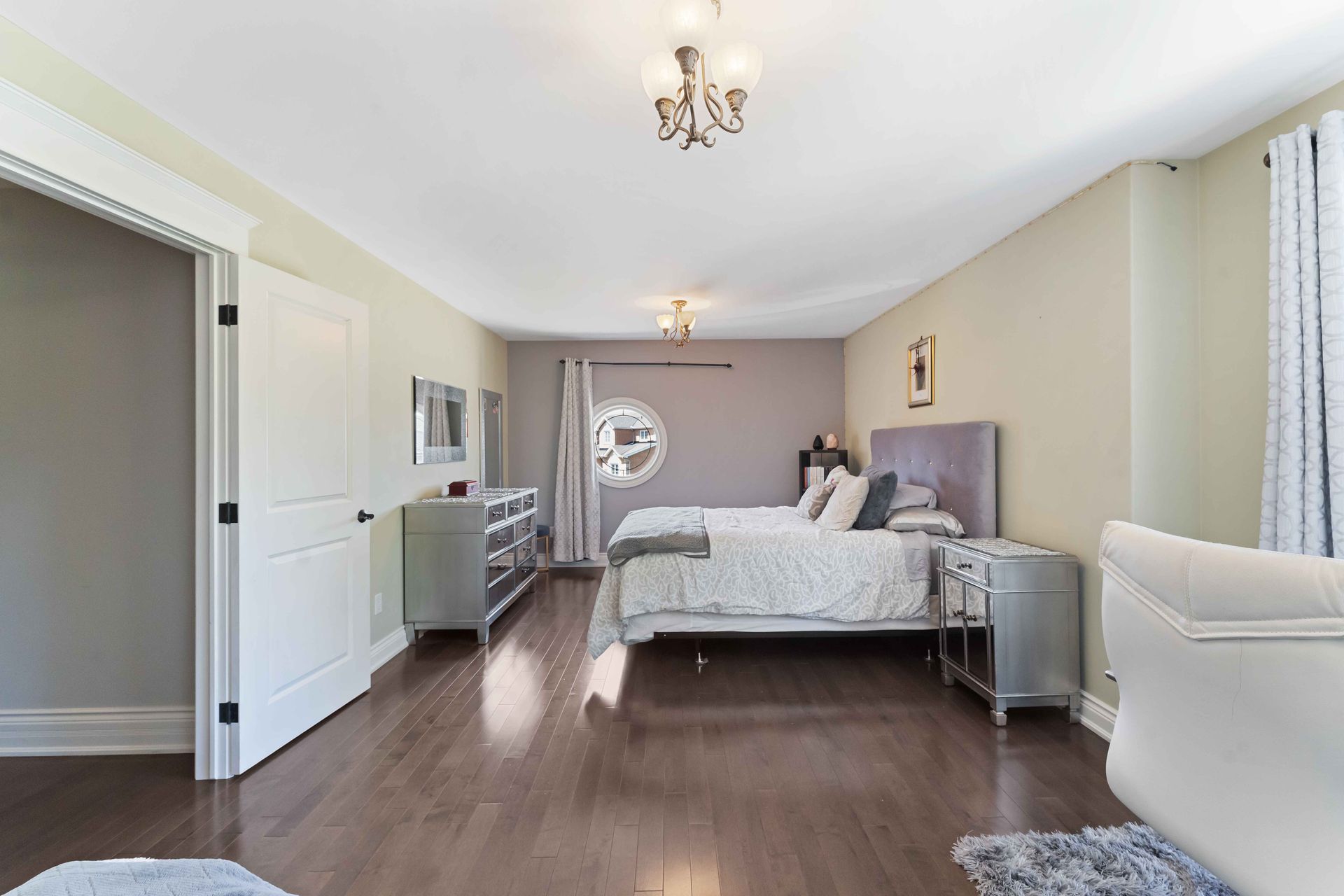 A large bedroom with a king size bed , dresser , nightstand , and chandelier.