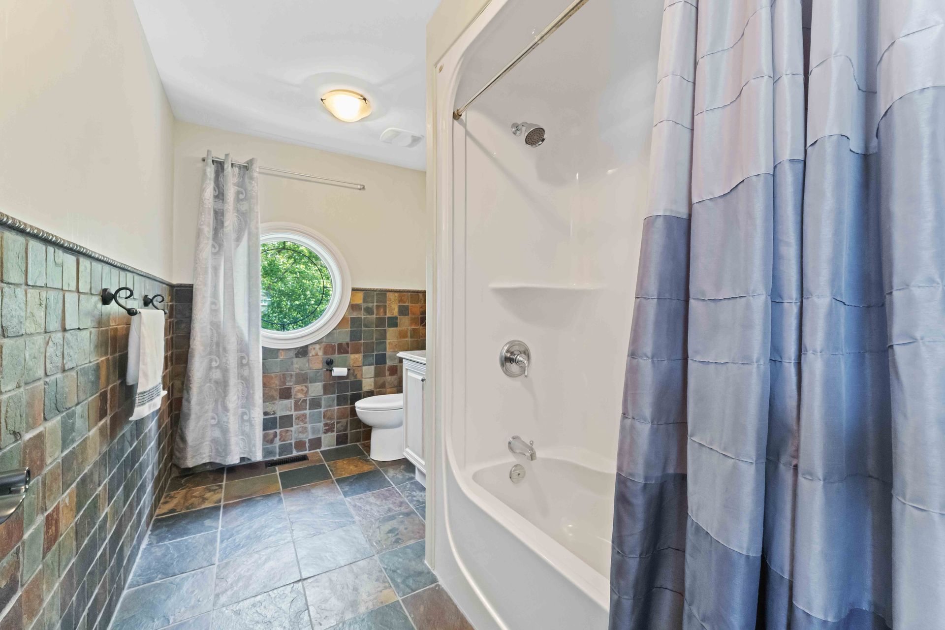 A bathroom with a tub , shower , toilet and window.