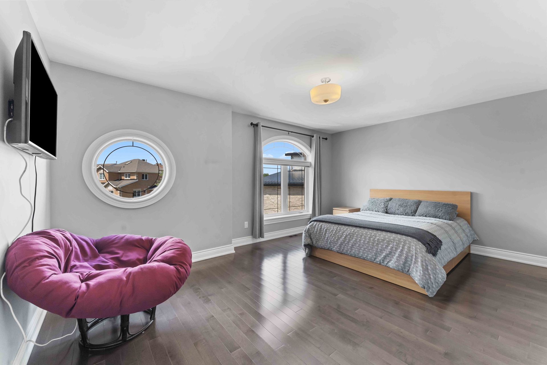 A bedroom with a bed , chair , television and a round window.