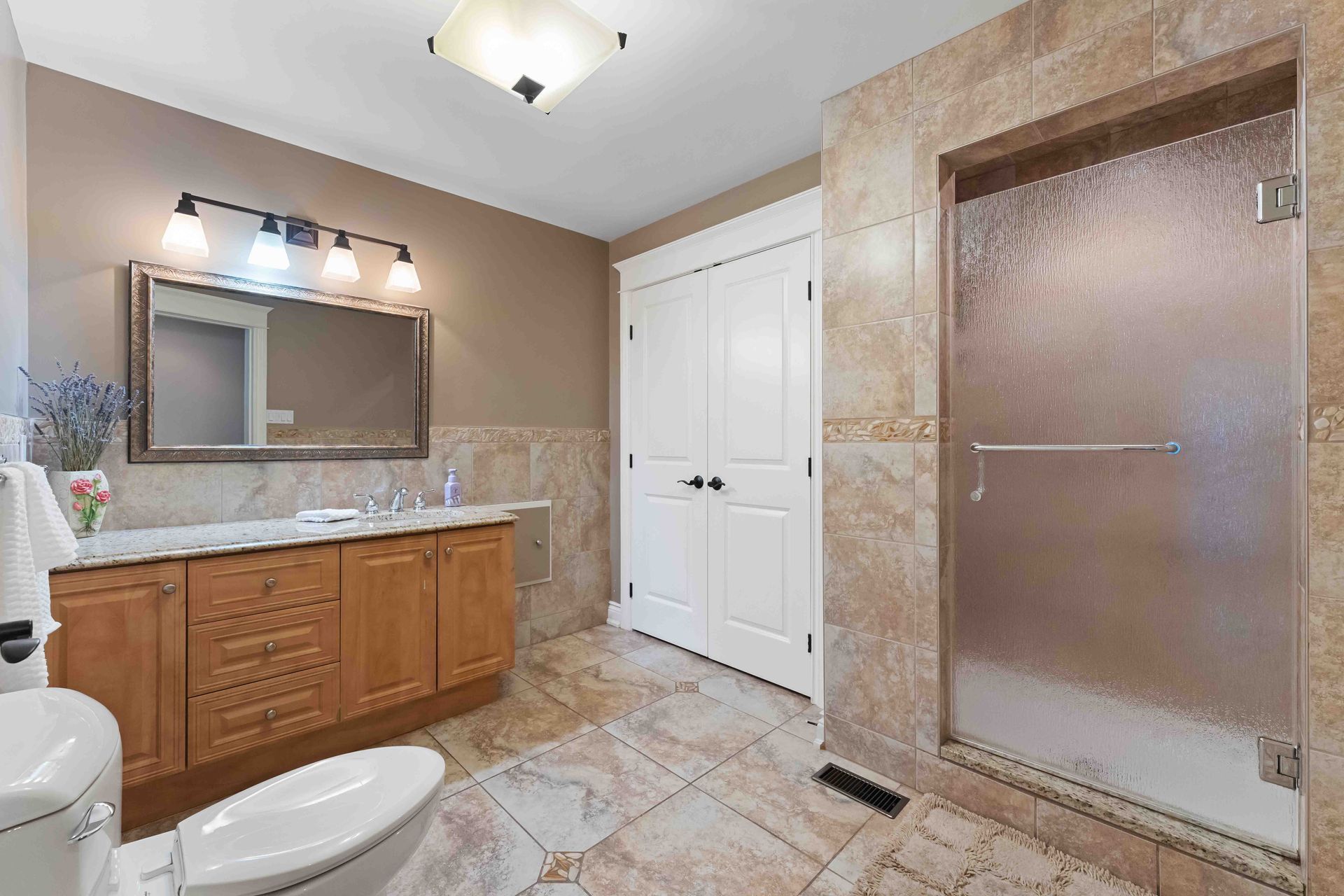 A bathroom with a toilet , sink , mirror and walk in shower.