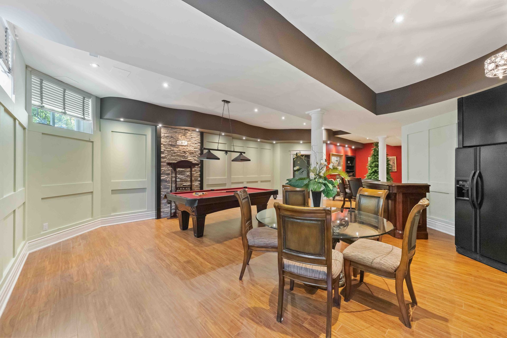 A basement with a pool table , dining table , chairs and a refrigerator.