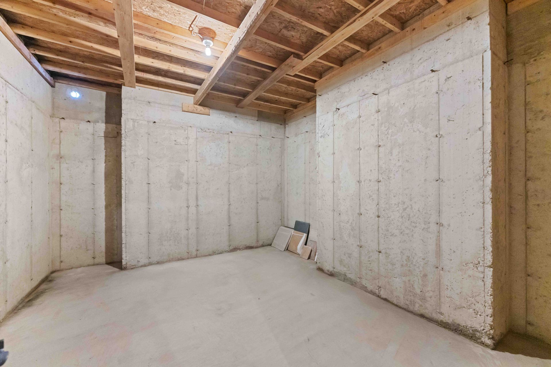 An empty basement with concrete walls and a wooden ceiling.