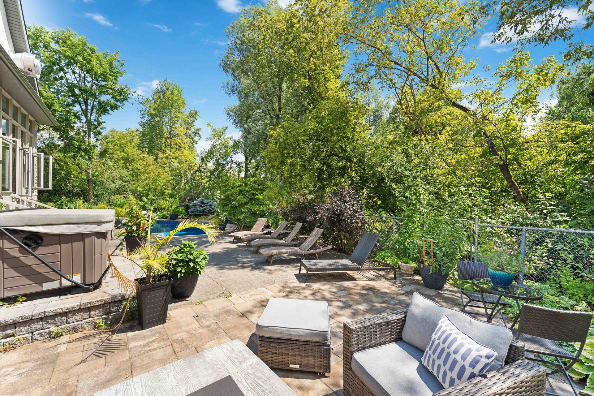 A patio with a couch , chairs and a hot tub surrounded by trees.