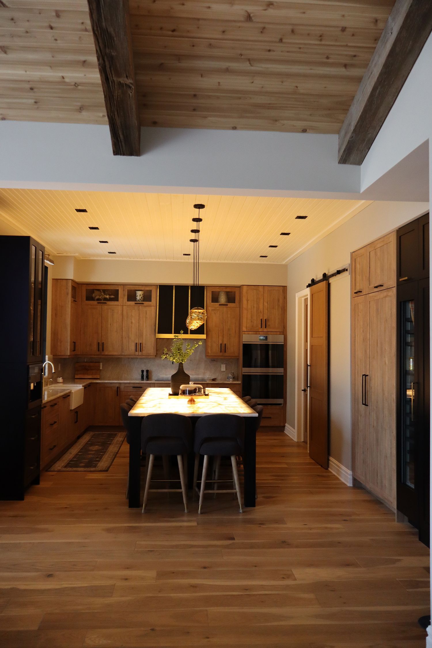 A kitchen with wooden cabinets , hardwood floors , a table and chairs.
