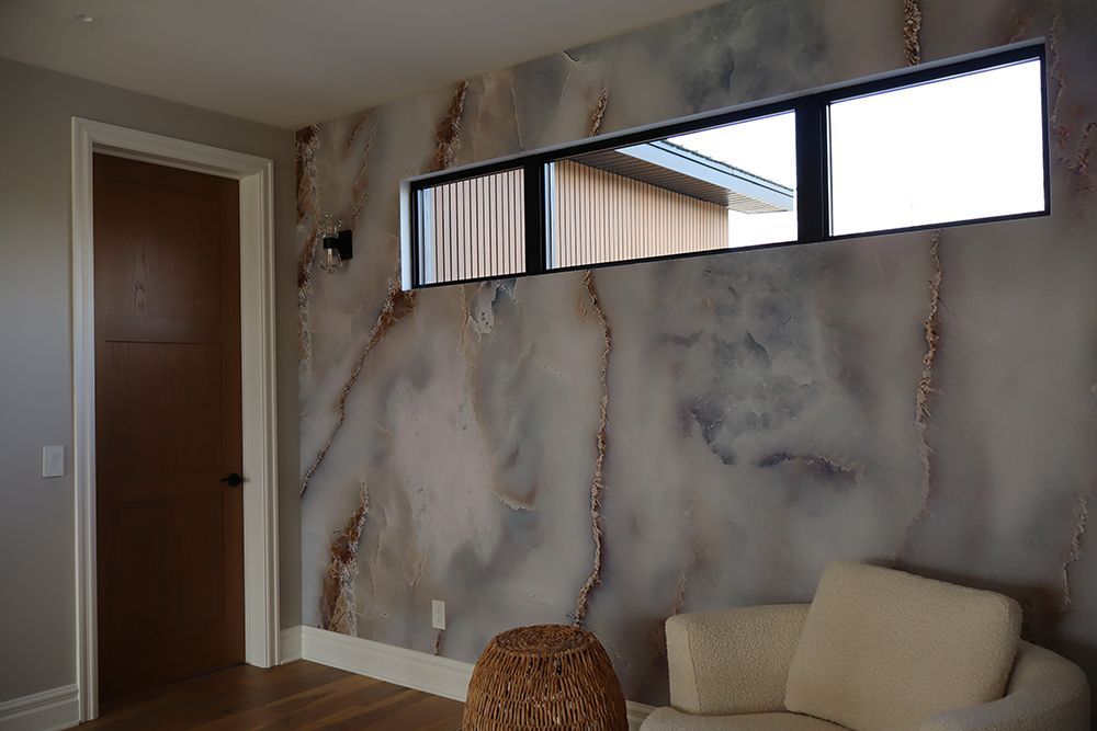 A living room with a couch and a window with a marble wall.