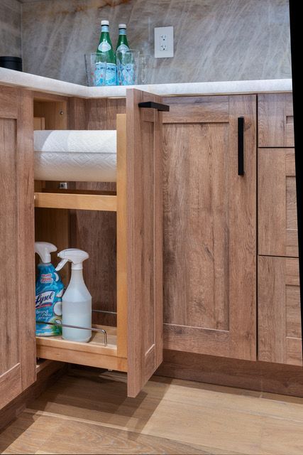 A kitchen cabinet with a pull out drawer filled with cleaning supplies.
