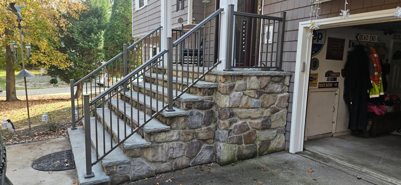 Stone steps with metal railings leading to a house porch next to an open garage.