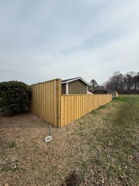 A new wooden fence encloses a backyard space with a small shed, seen from an outdoor, grassy yard on a cloudy day.