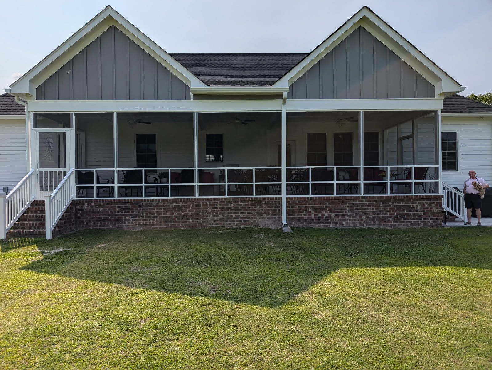 A back view of a white home with a large, screened-in porch, a brick foundation, and two matching gabled roof sections.