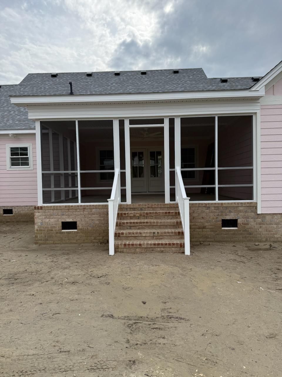A newly constructed house with pink siding and a central screened porch featuring white railings and brick steps.