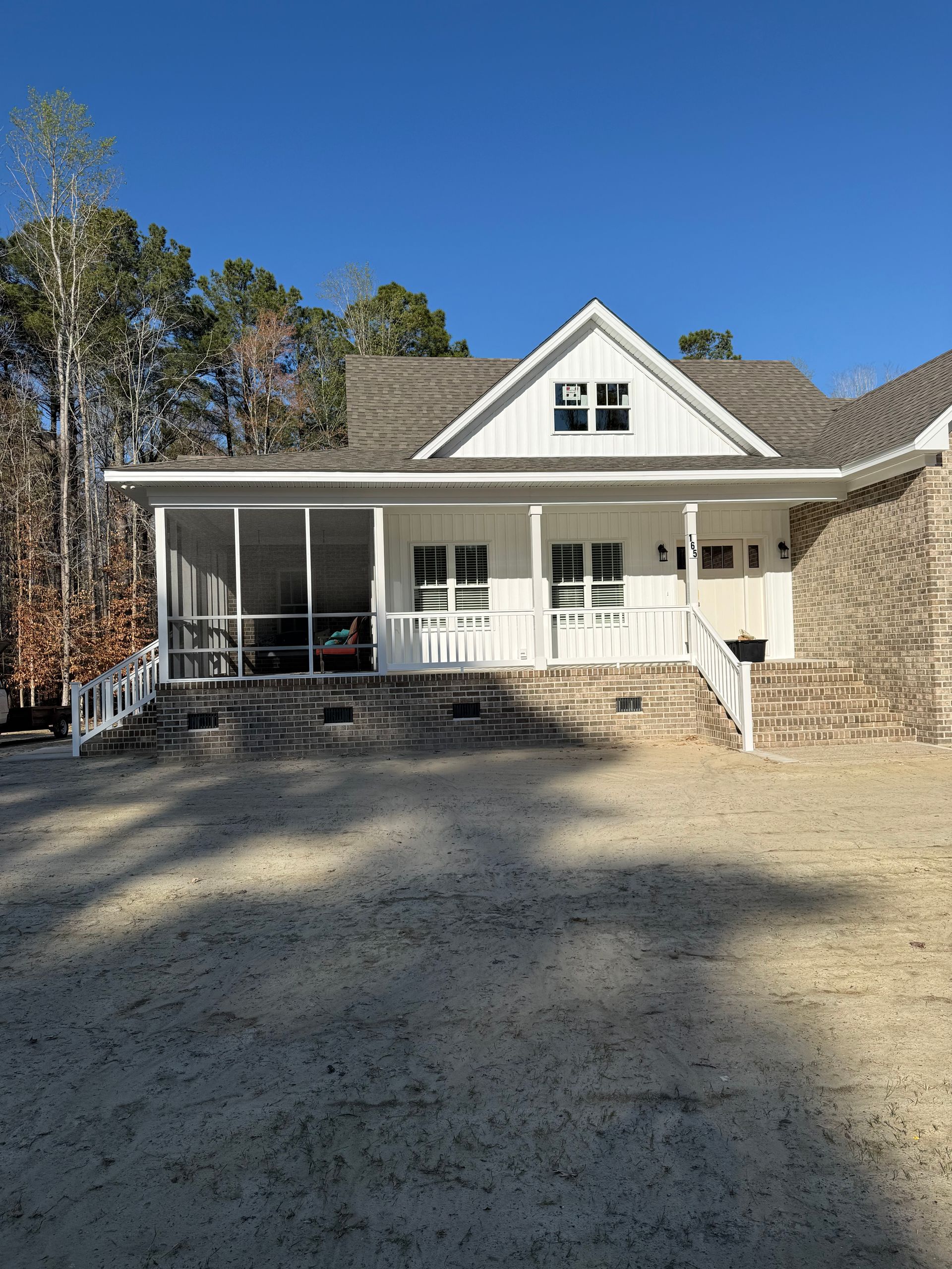 A white house with a screened-in porch and stone foundation under a clear blue sky.