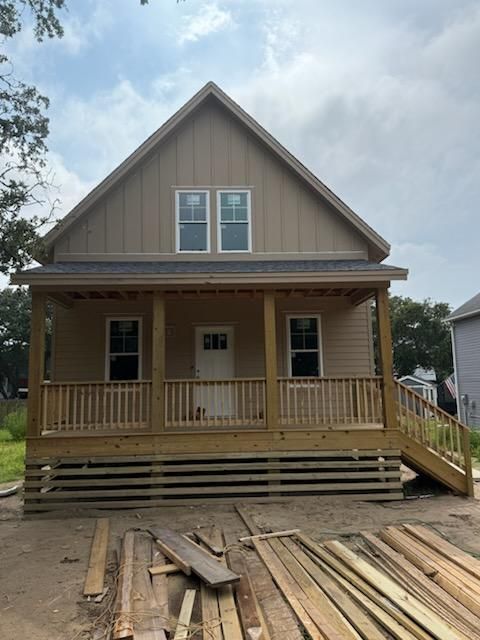 A tan house under construction with a front porch, wooden railings, and scattered lumber in the foreground.