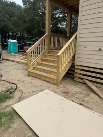 A new wooden staircase with railings leads to the deck of a light-colored house at a construction site.