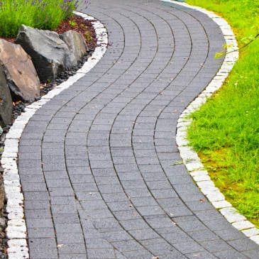 A curved brick walkway in a garden surrounded by grass and rocks.