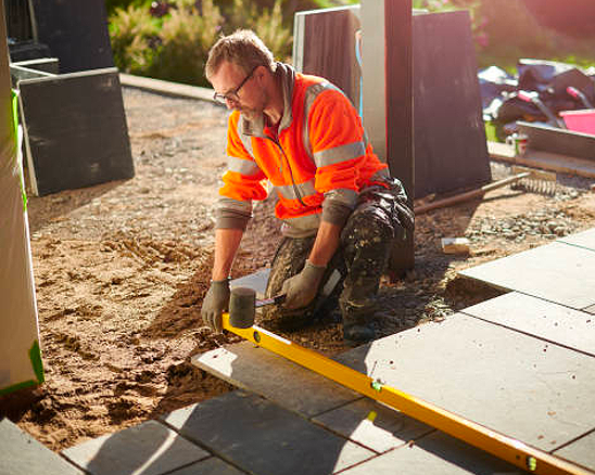 A man is kneeling down on the ground while working on a patio.