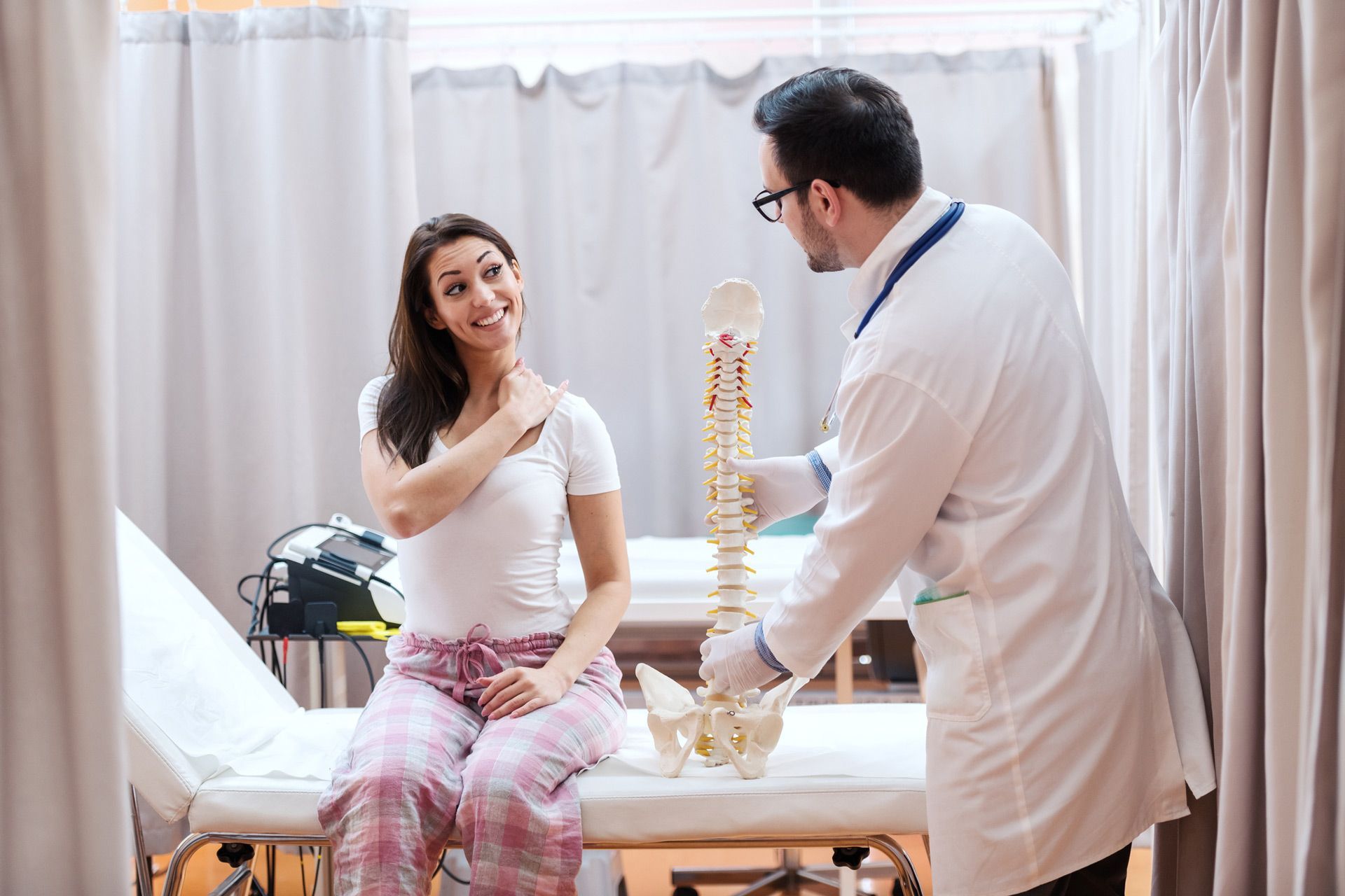 A doctor is holding a model of a spine while talking to a patient