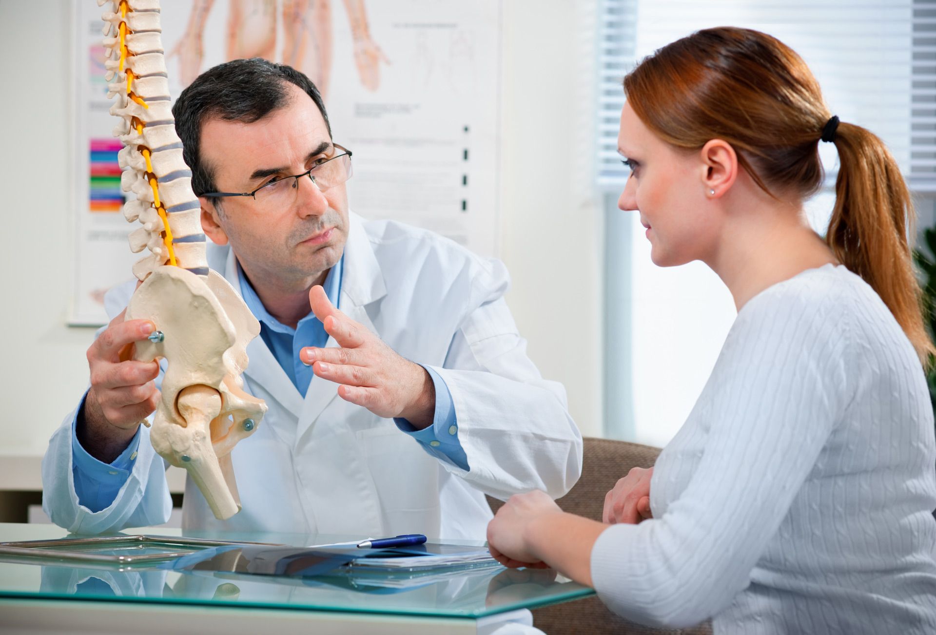 A doctor is talking to a patient while holding a model of a spine
