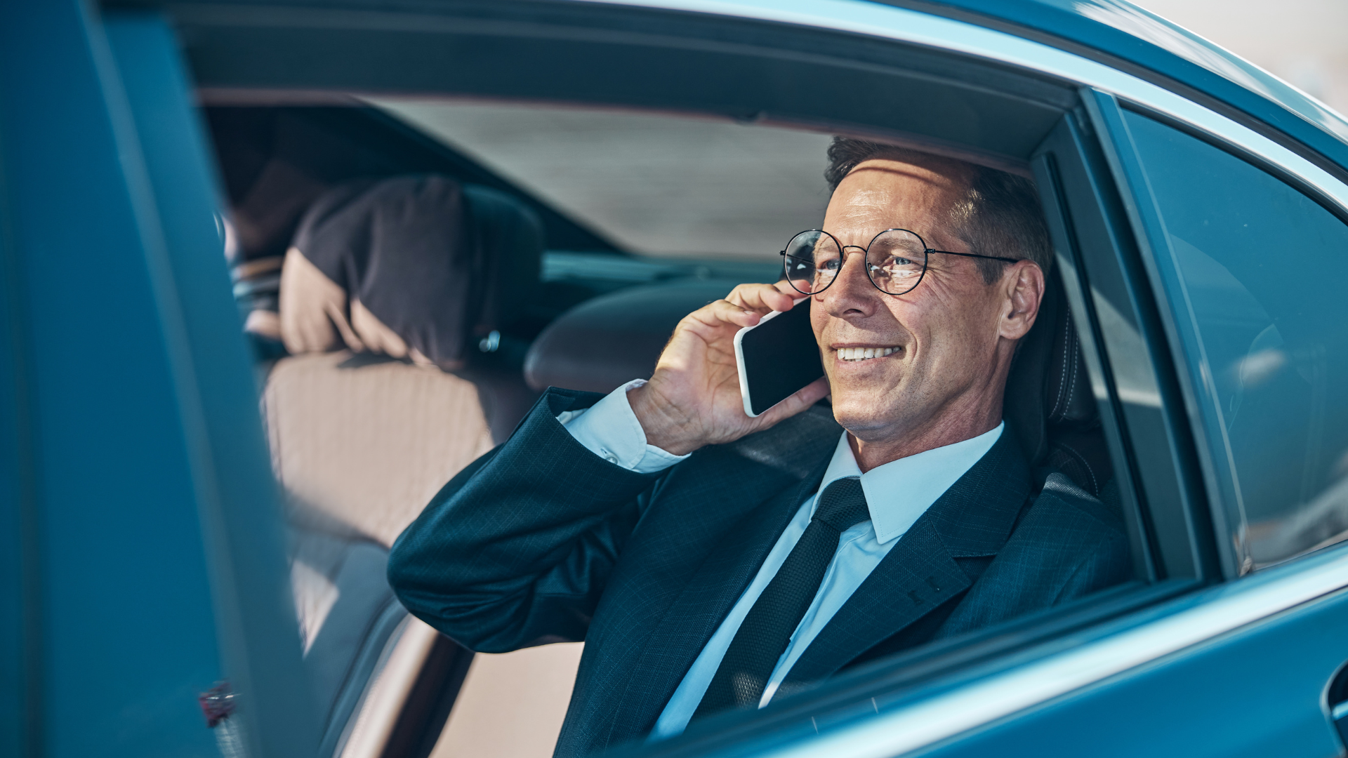 A man in a suit and tie is sitting in a car talking on a cell phone.
