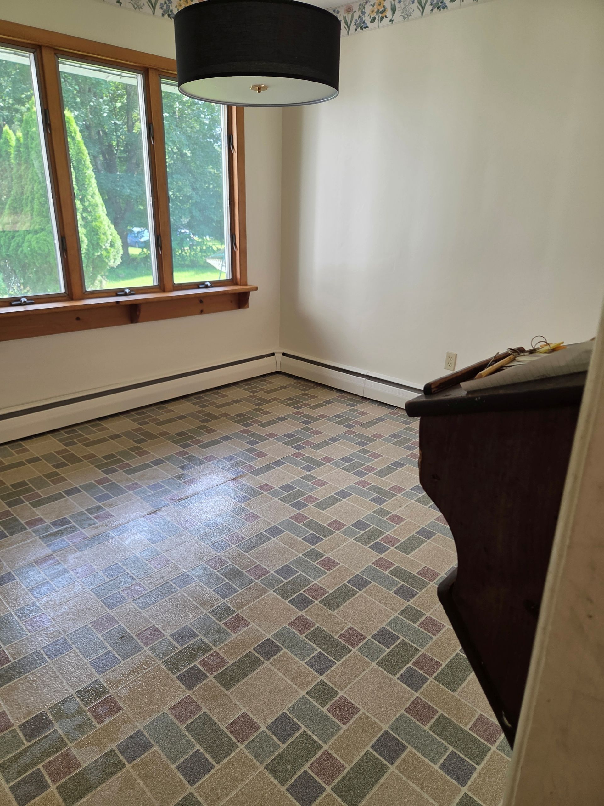 Room with patterned flooring, large window, dresser, and black light fixture.