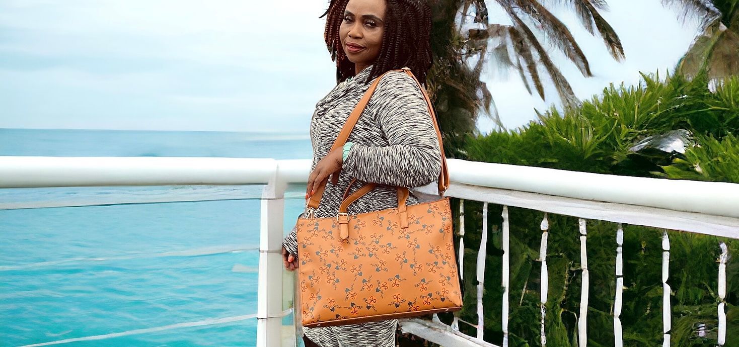 A woman is standing on a balcony overlooking the ocean holding a purse.