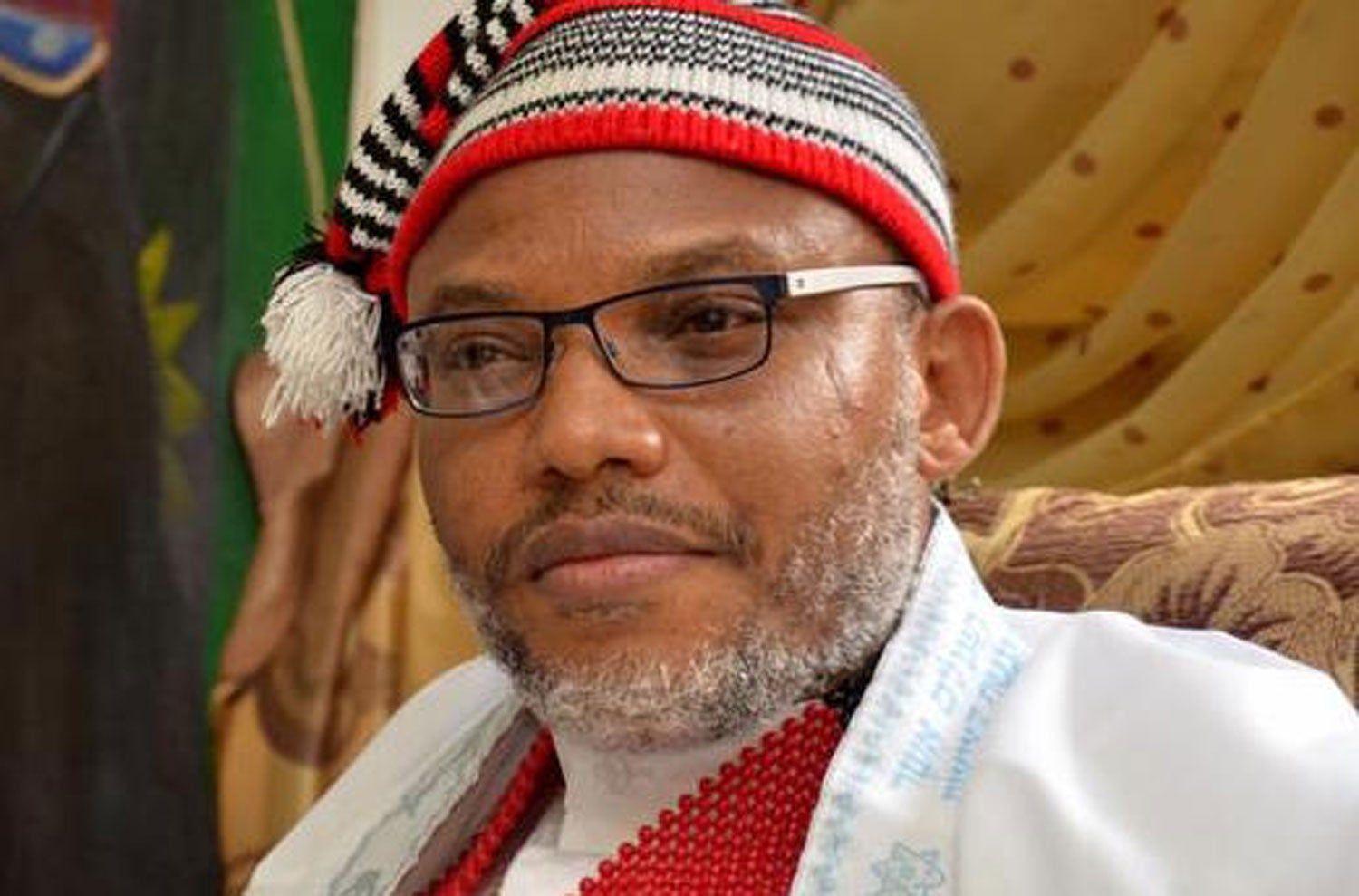 A man wearing a red and white hat and glasses is sitting on a couch.