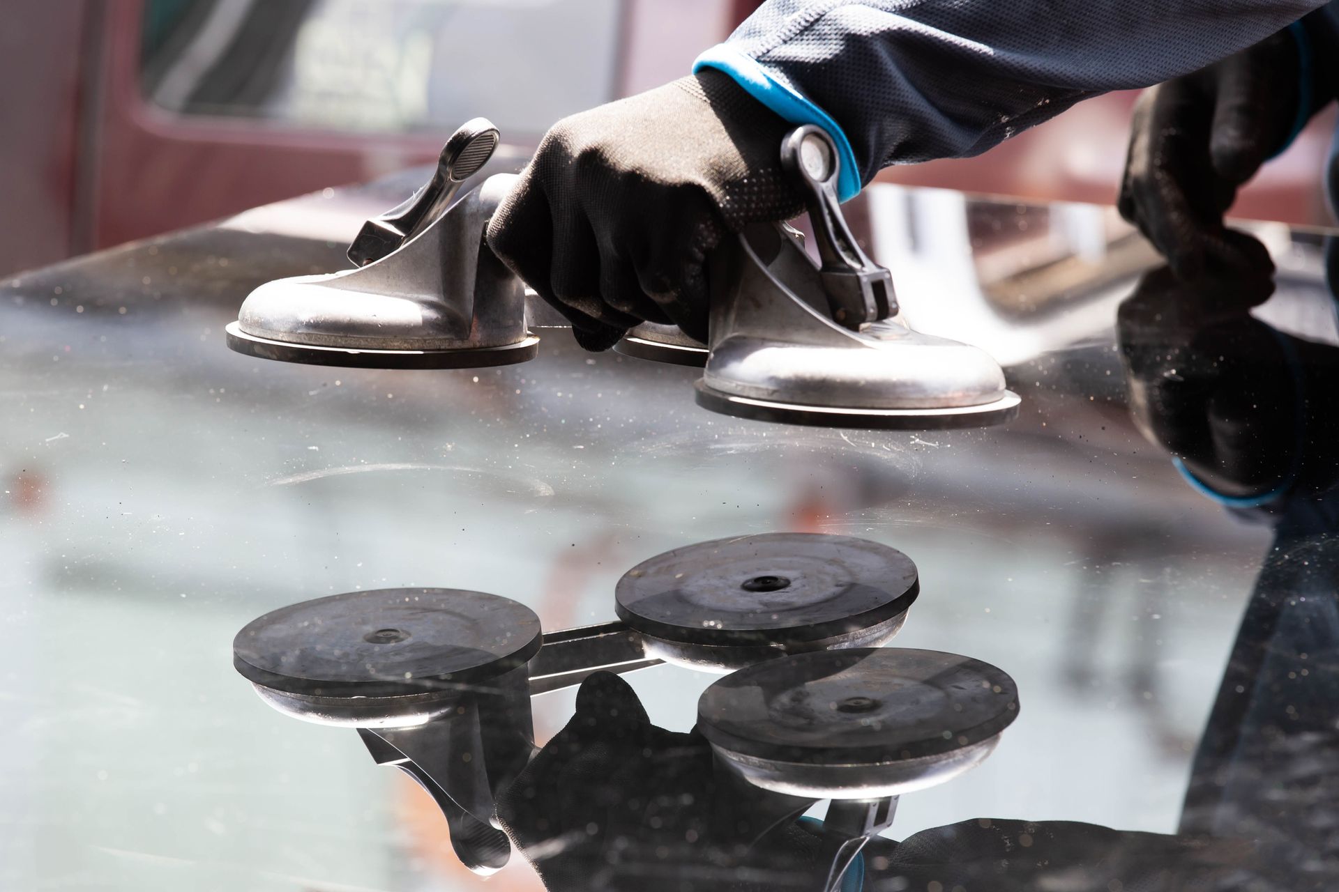 Person using suction cups to lift a sheet of glass, wearing gloves; indoors.