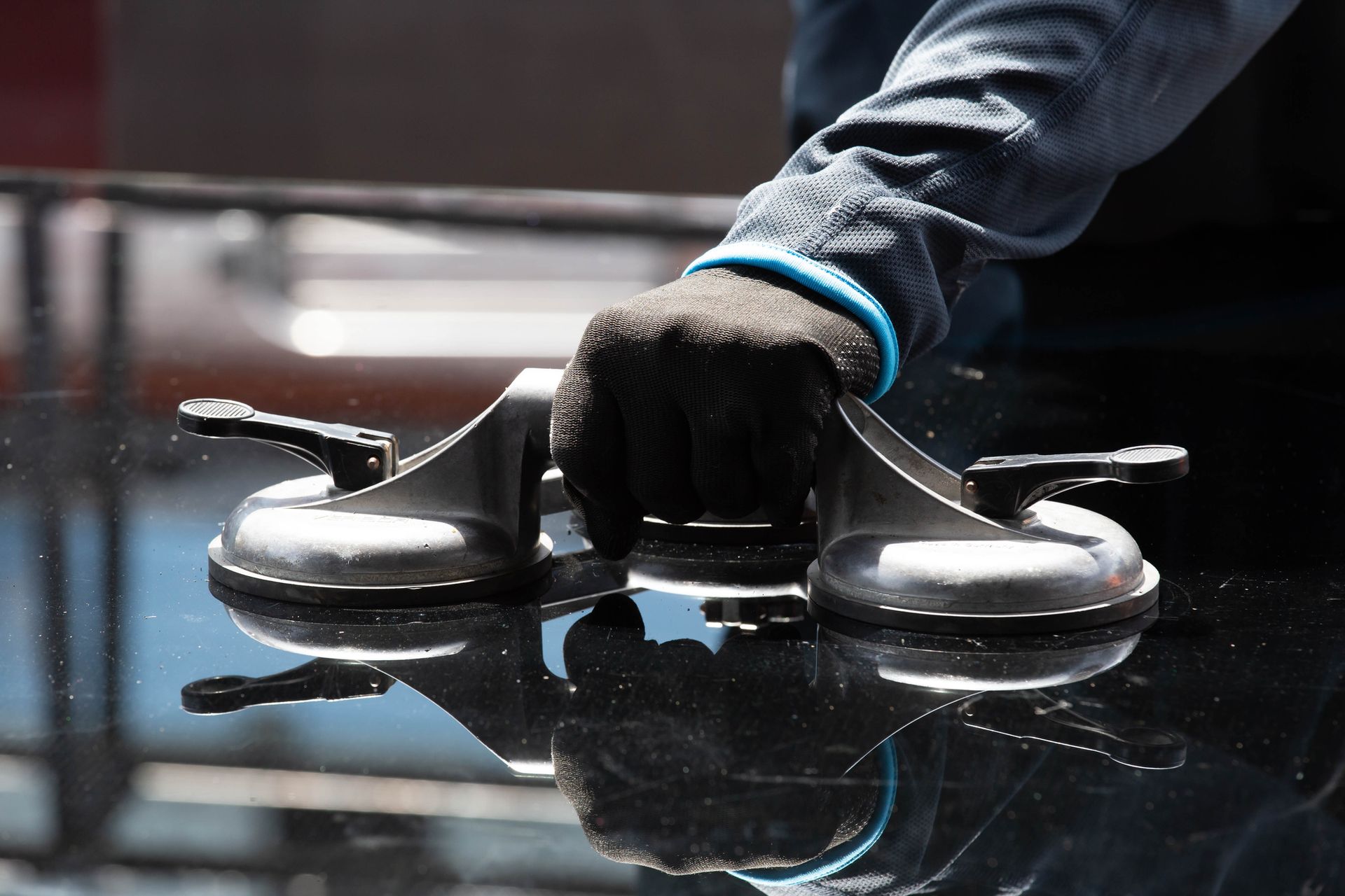 A gloved hand uses suction cups to lift a sheet of dark glass.