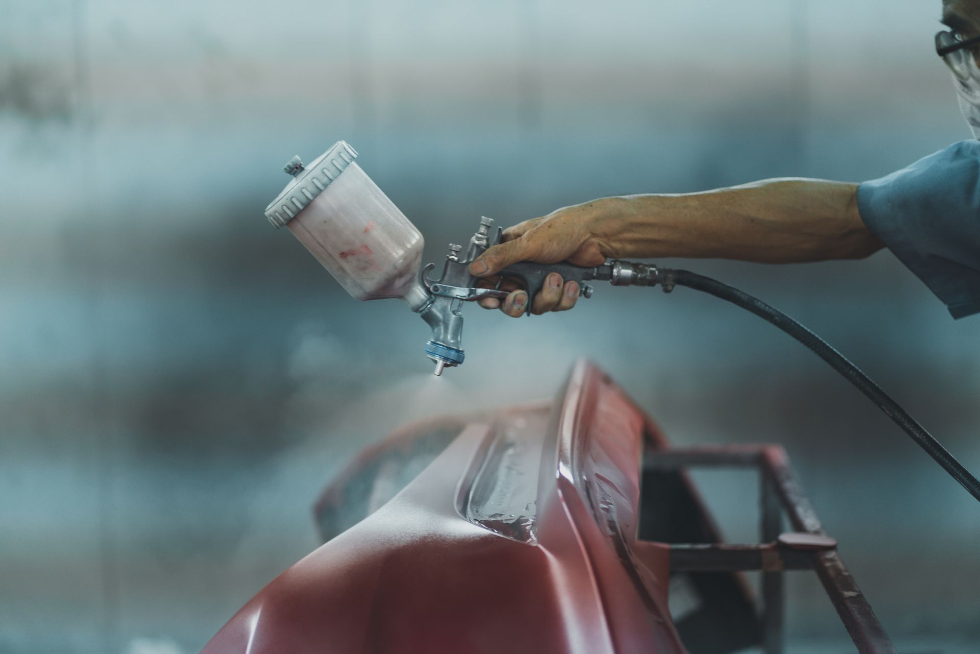Person spraying red paint on car bumper.