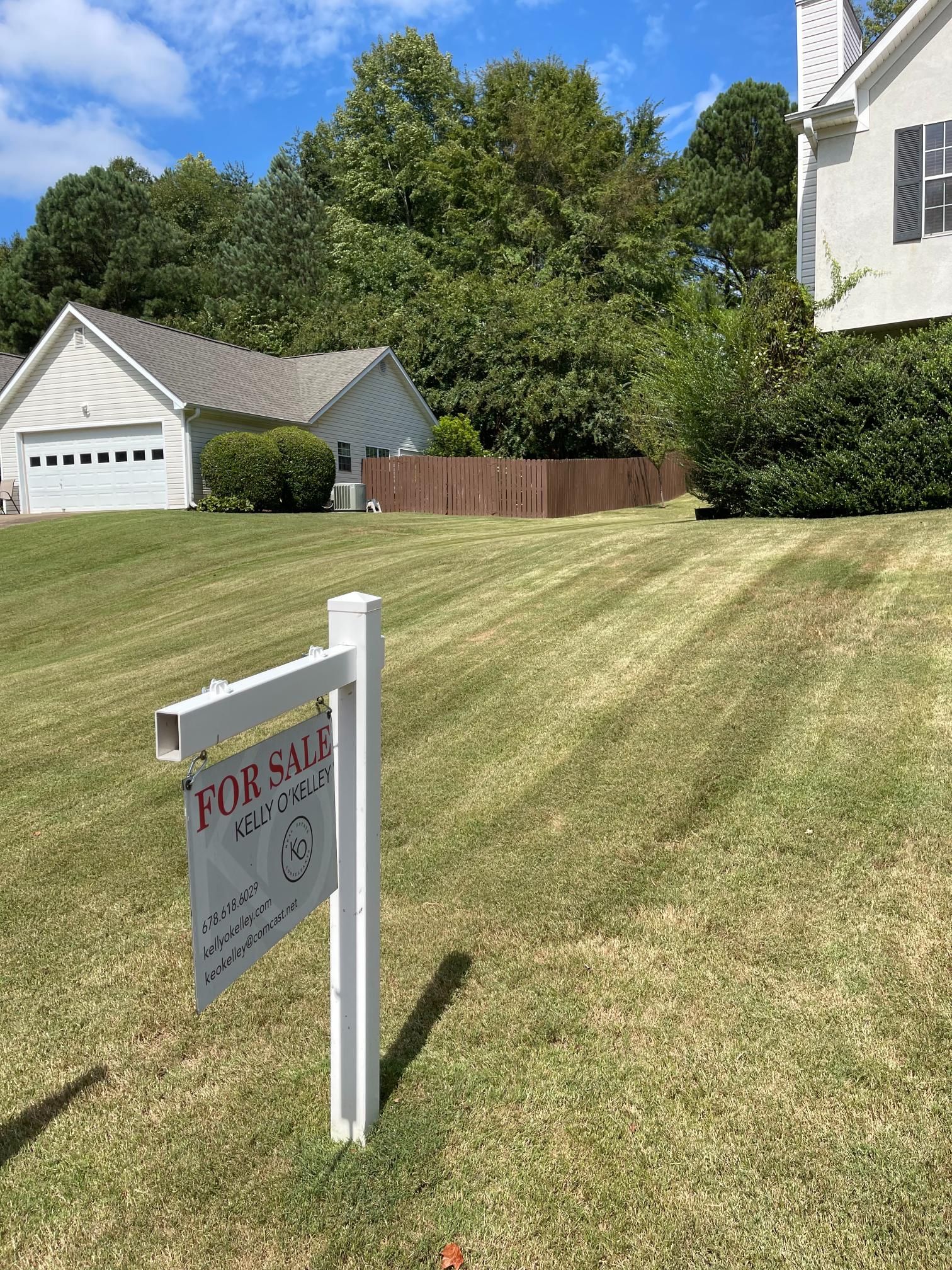 A for sale sign is sitting in the grass in front of a house.