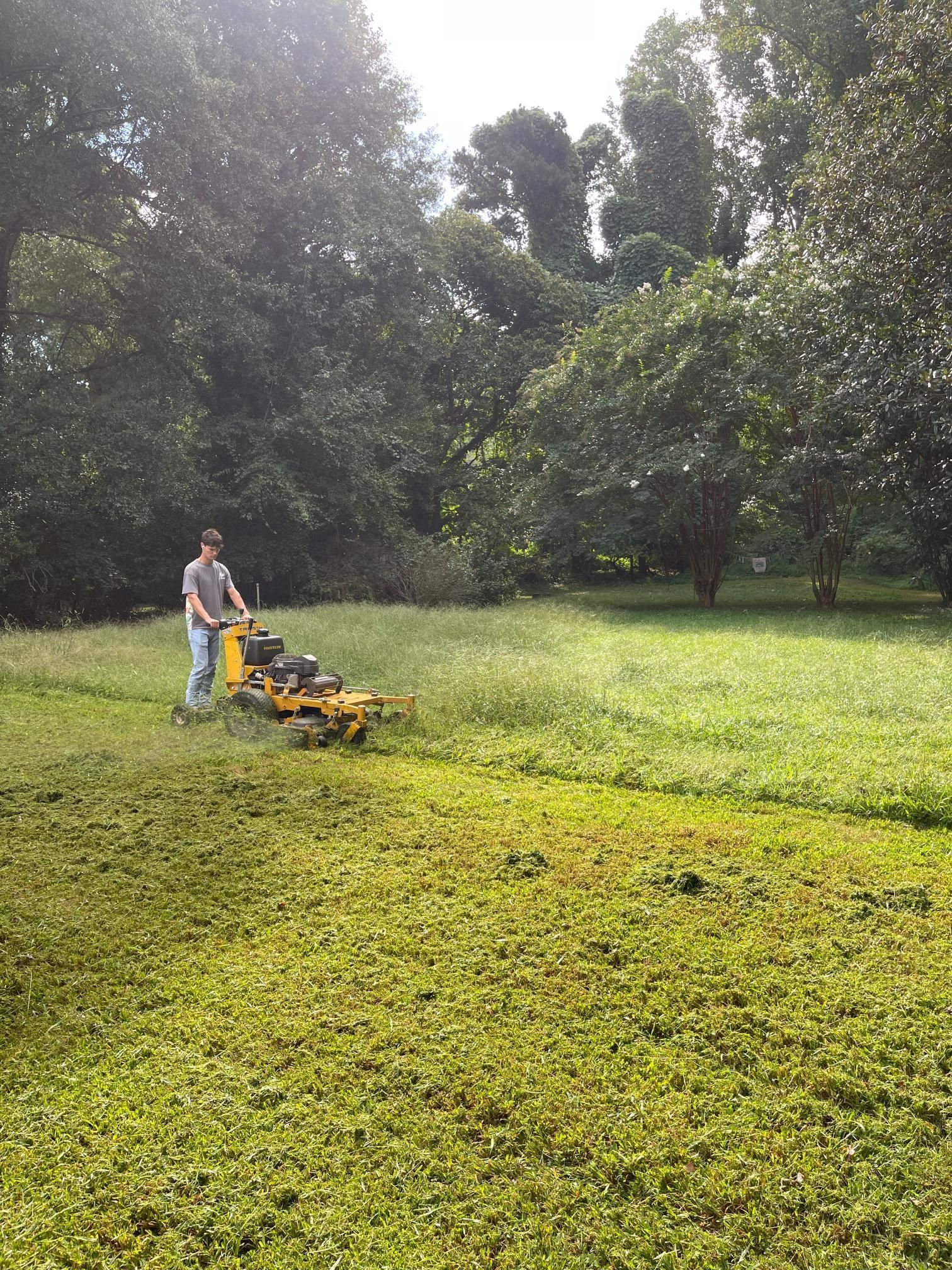 A man is mowing a lush green field with a yellow lawn mower.