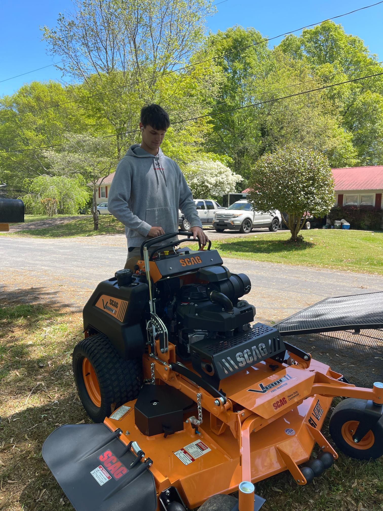 A man is standing next to a lawn mower in a driveway.