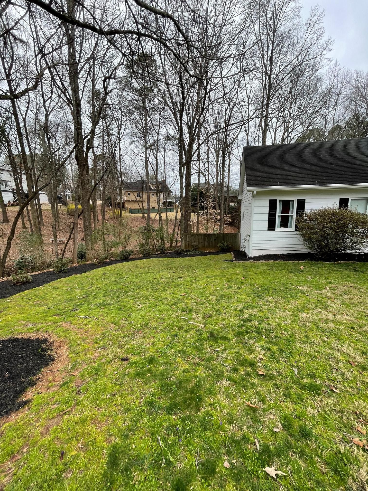 A white house is sitting in the middle of a lush green yard surrounded by trees.