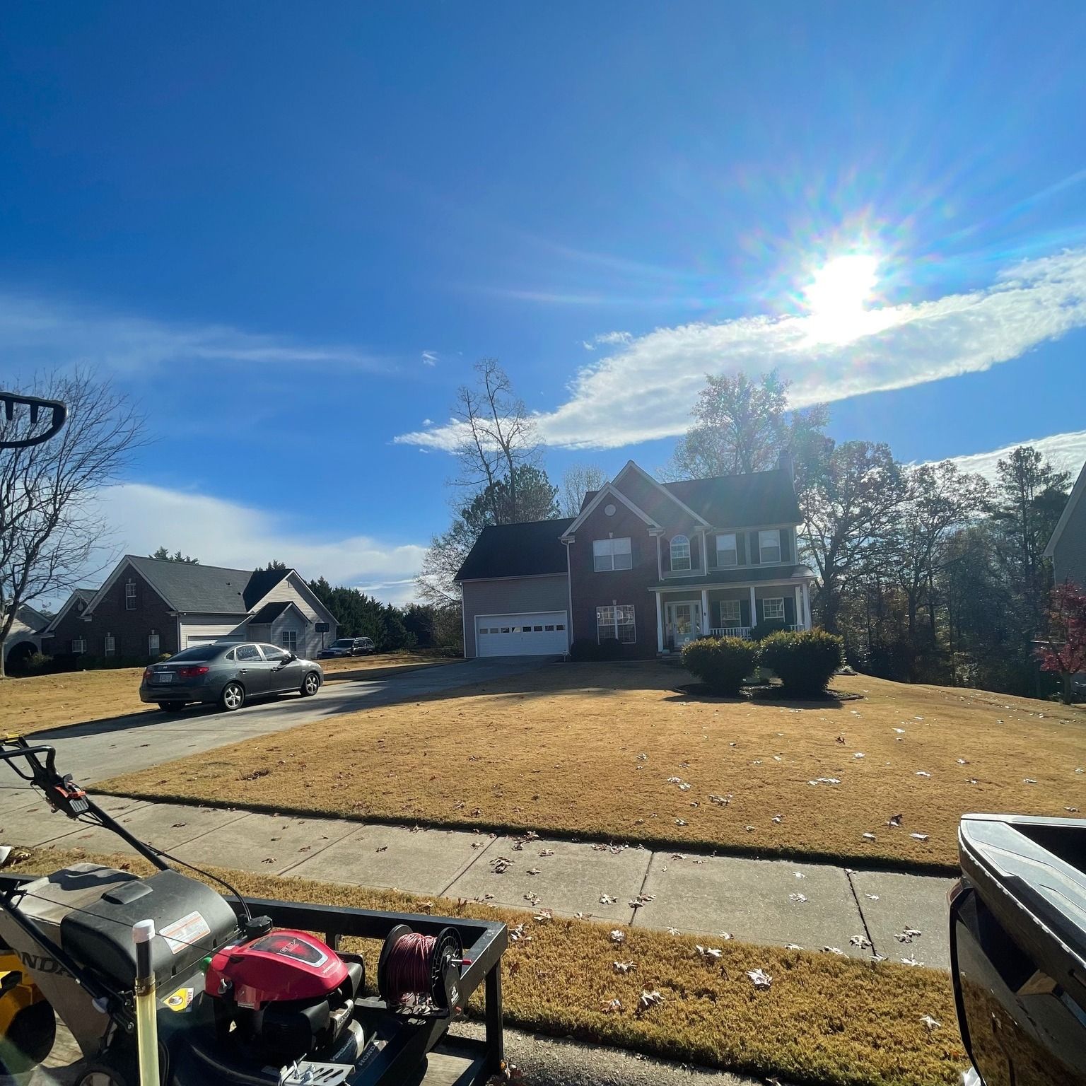 A lawn mower is parked in front of a house on a sunny day.