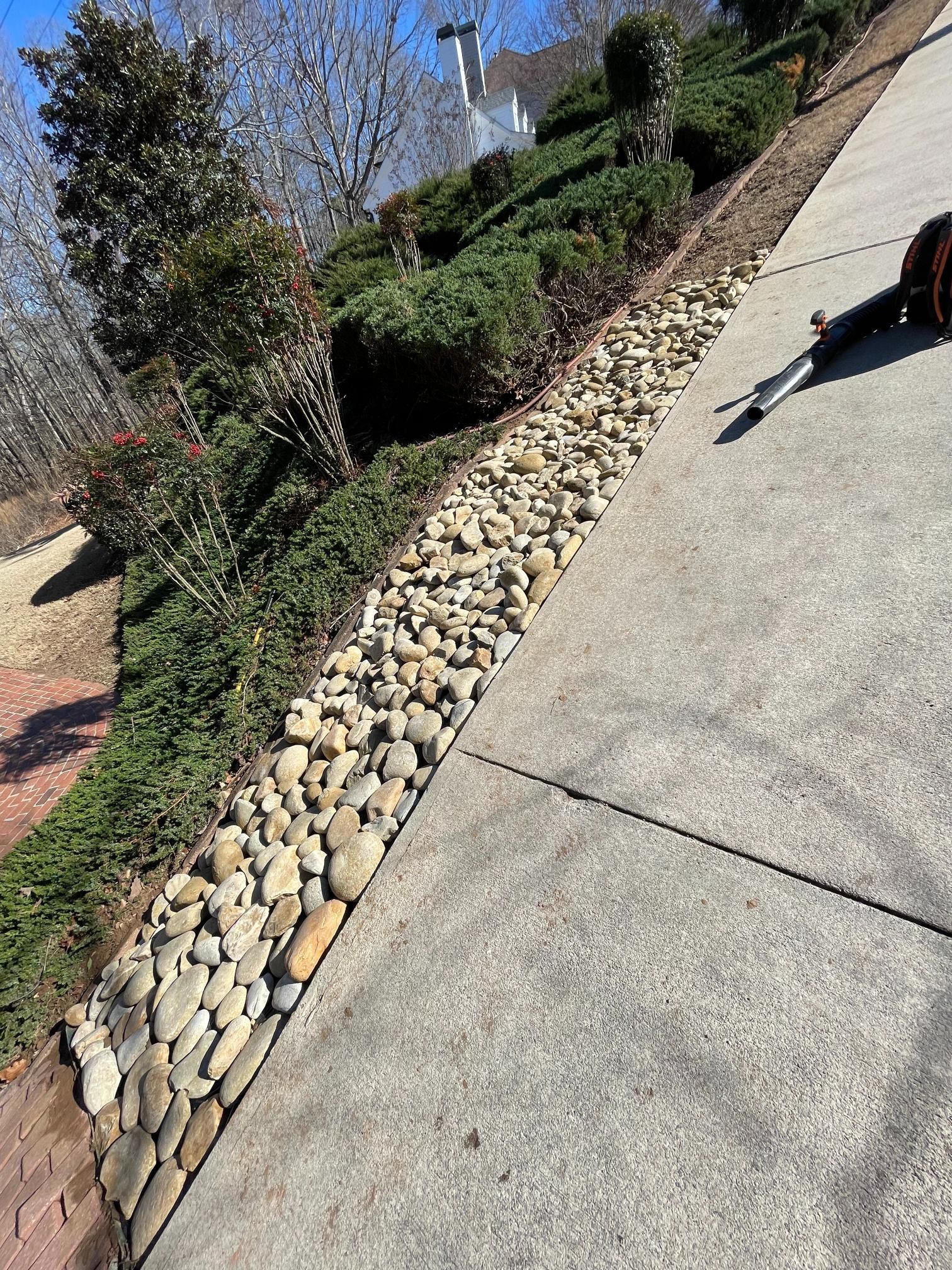 A person is standing on a sidewalk next to a pile of rocks.