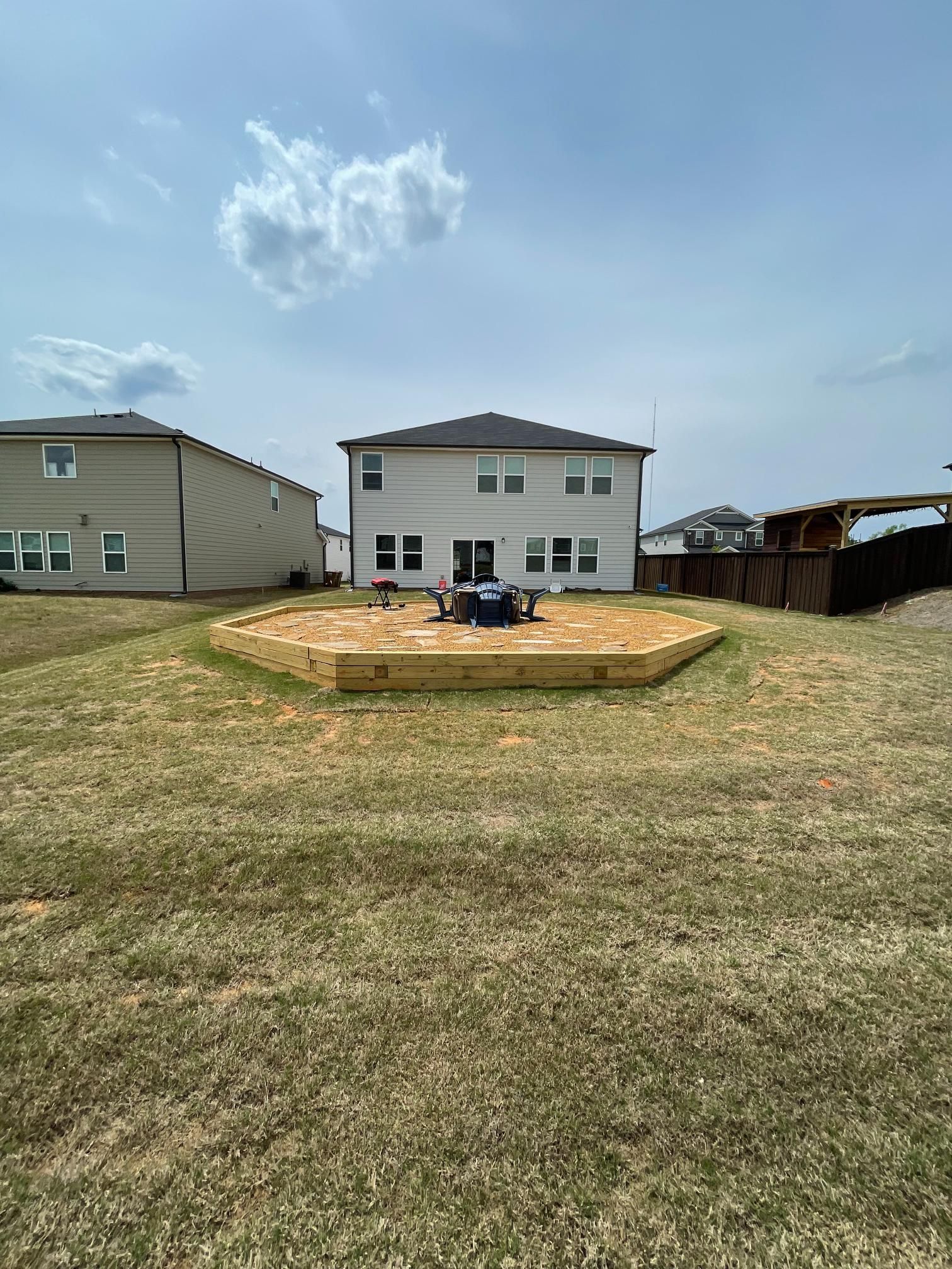 A wooden deck is sitting in the middle of a lush green field in front of a house.