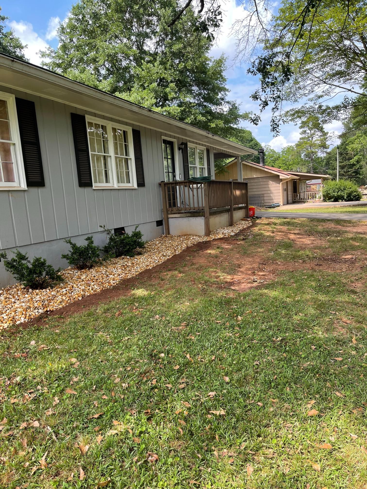 A white house with black shutters and a large lawn in front of it.