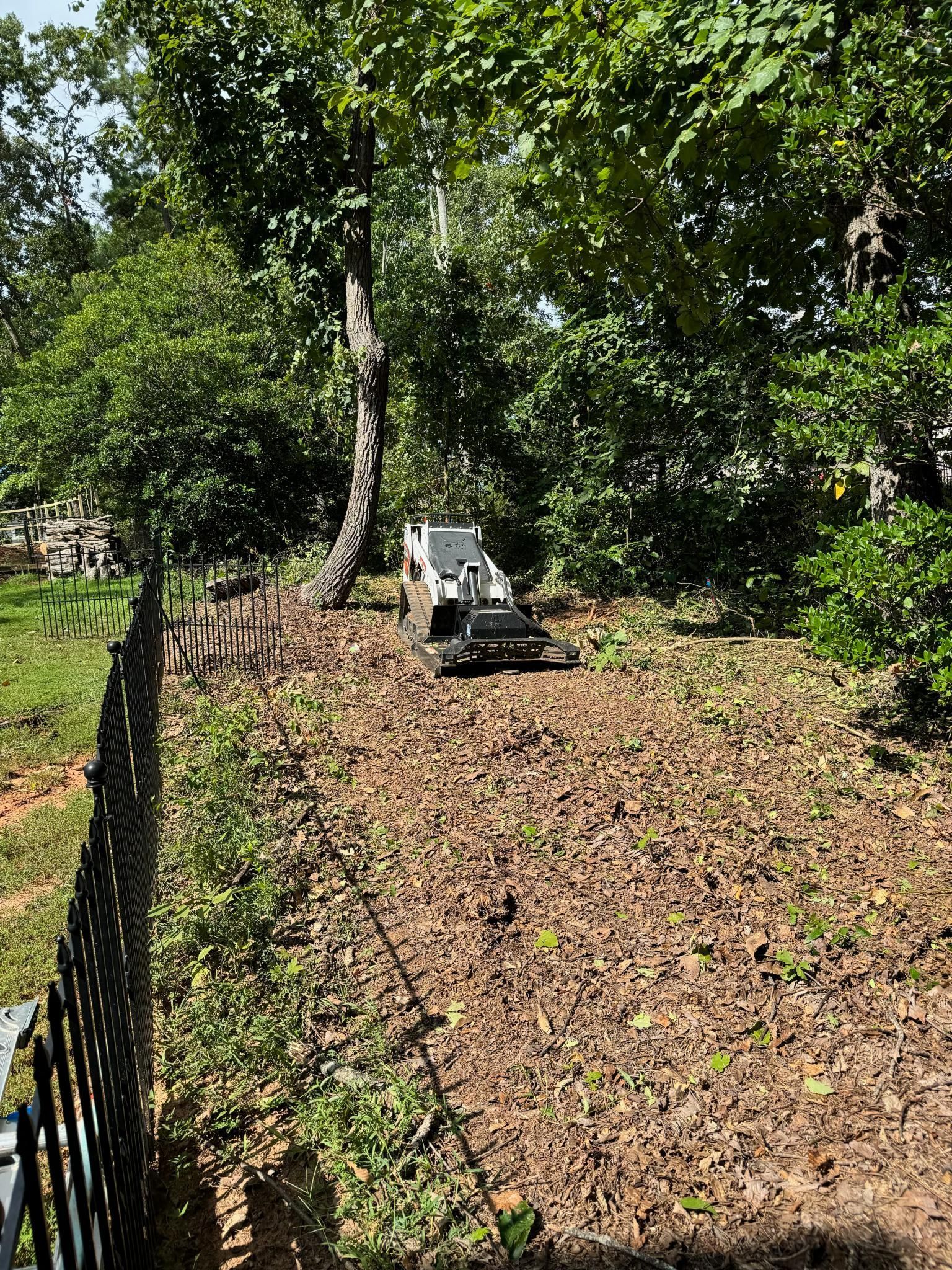 A stump grinder is sitting in the middle of a yard next to a fence.