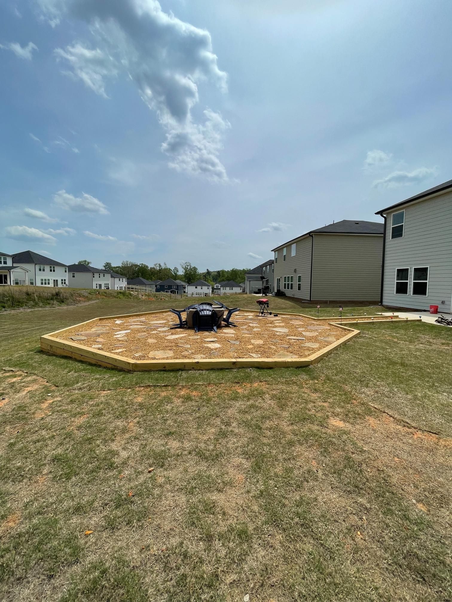 A fire pit is sitting in the middle of a grassy field in front of a house.