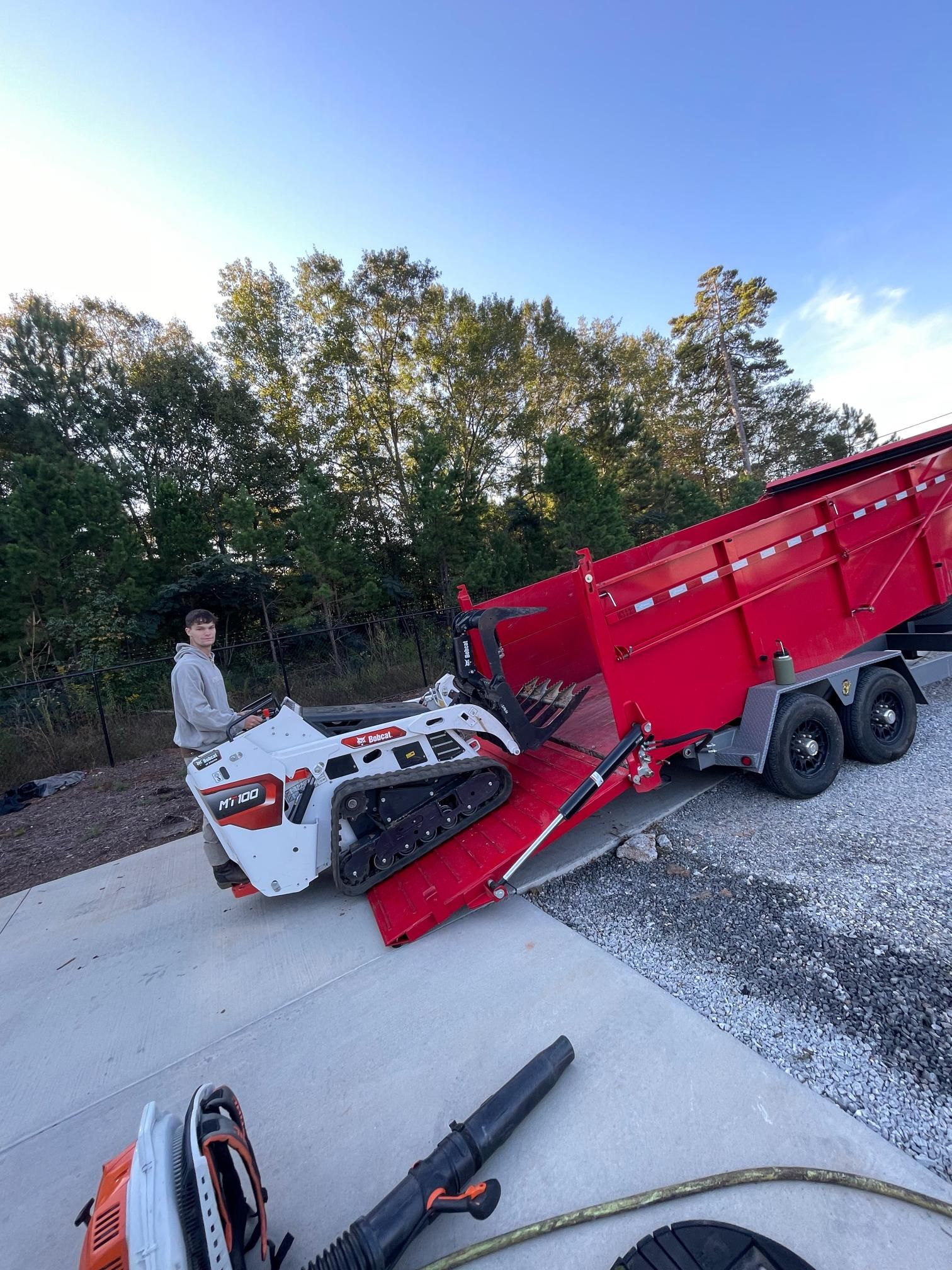 A man is standing next to a red trailer with a tractor on it.