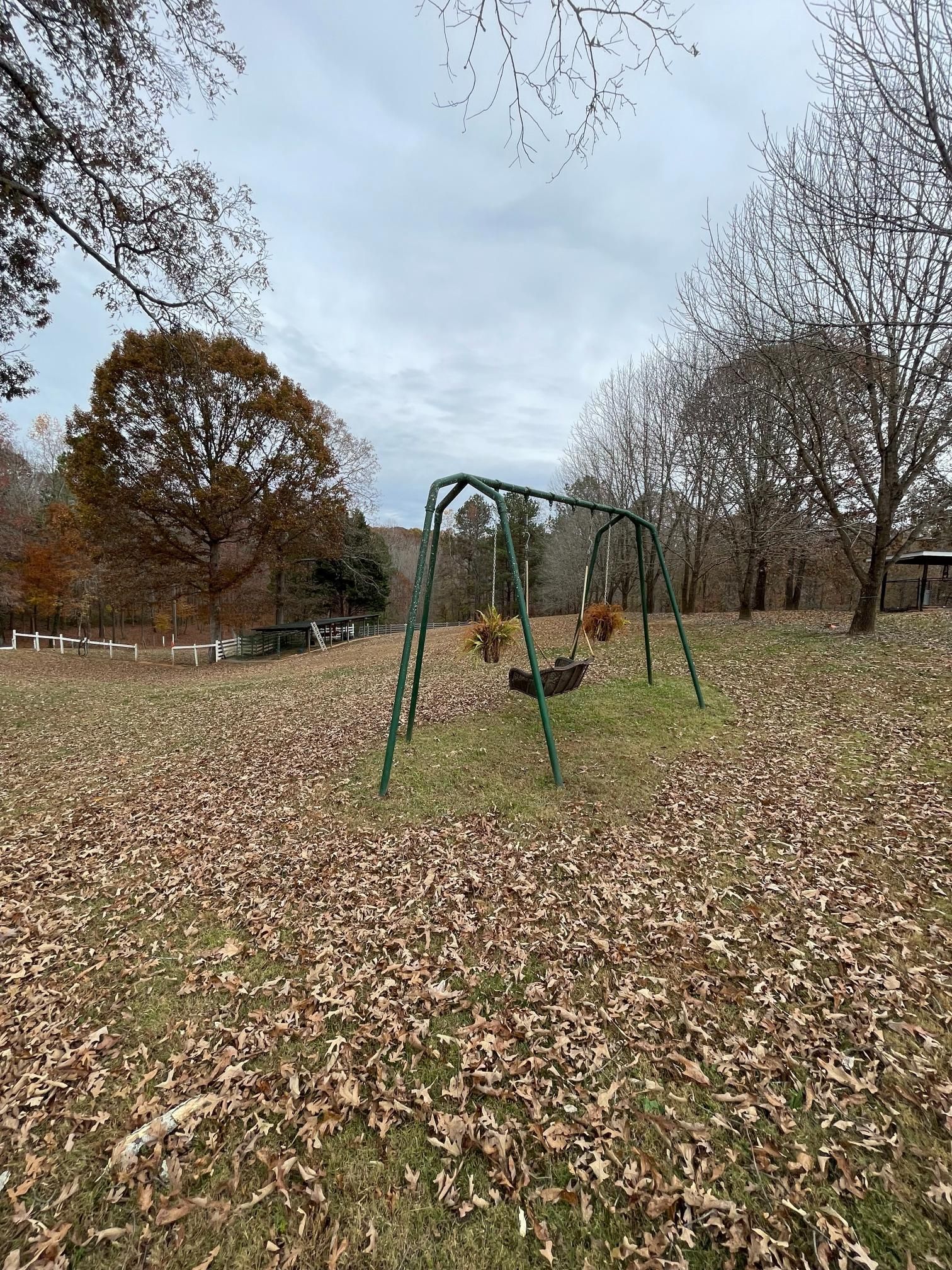 A swing set is sitting in the middle of a field covered in leaves.