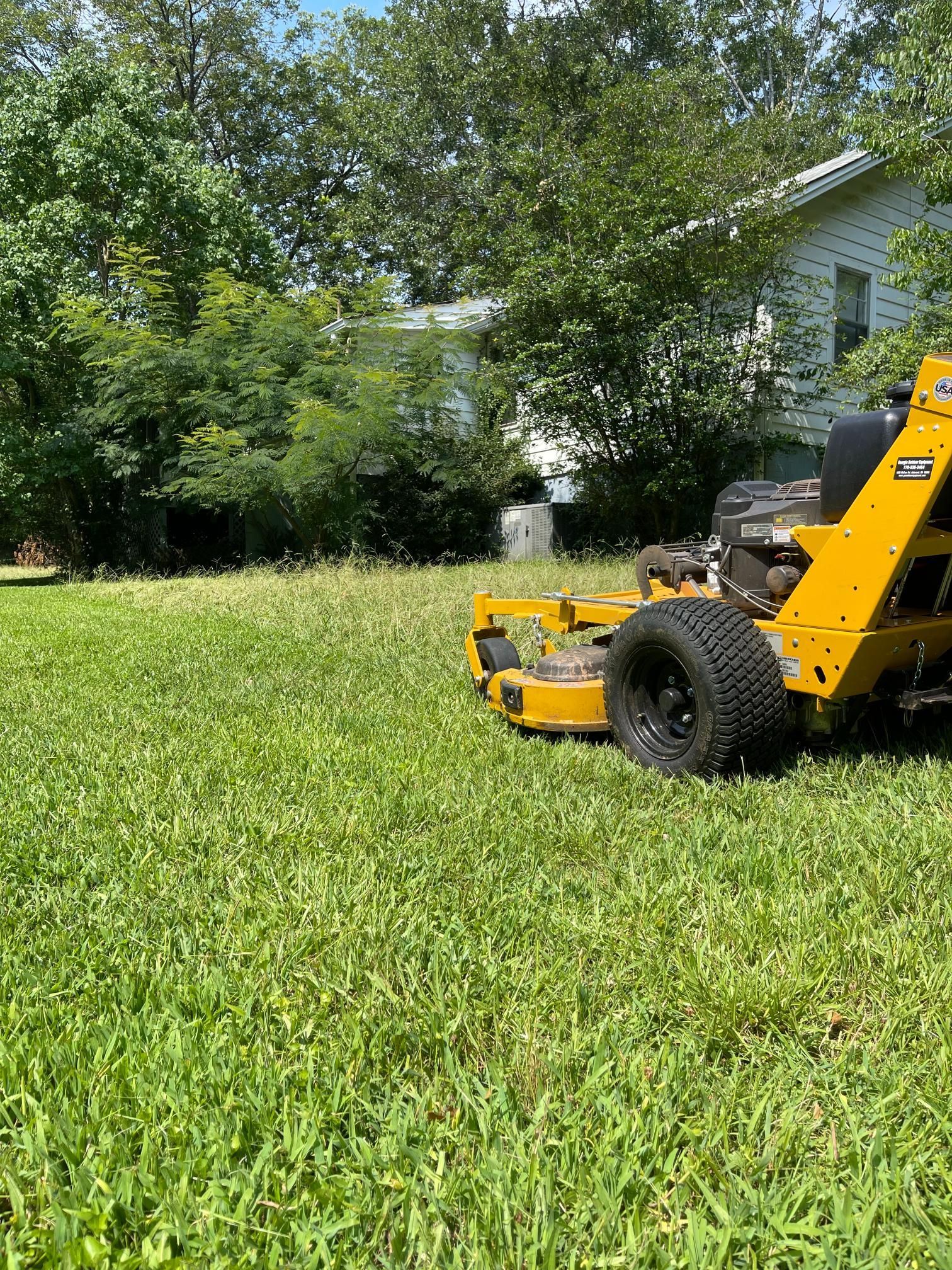 A yellow lawn mower is cutting a lush green lawn in front of a house.