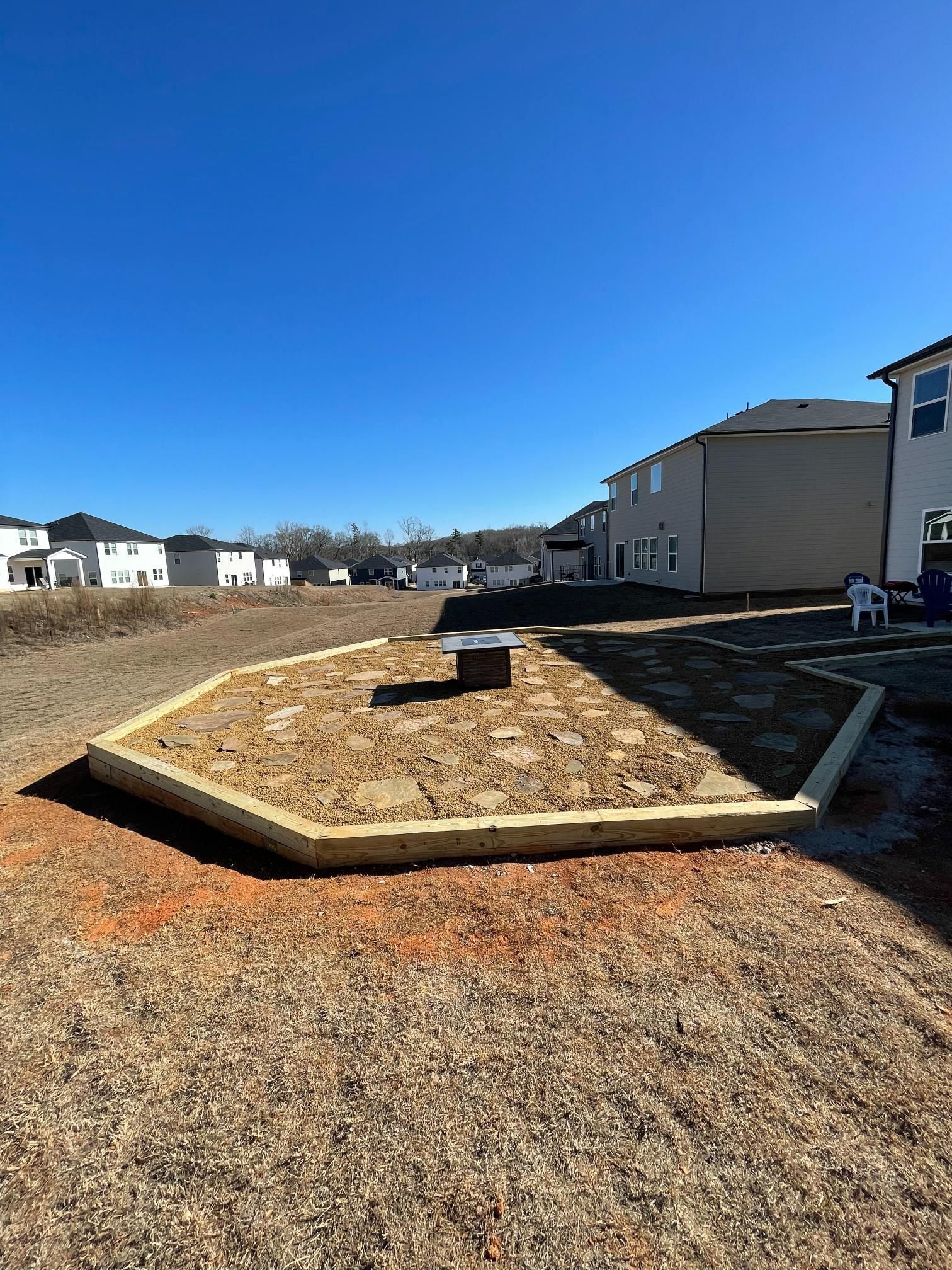 A wooden fence is sitting in the middle of a dirt field in front of a house.