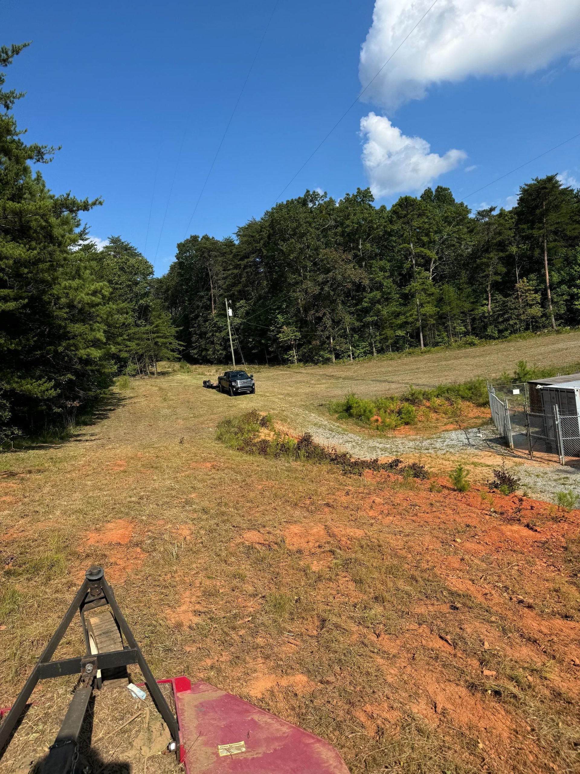 A car is driving down a dirt road in a field with trees in the background.