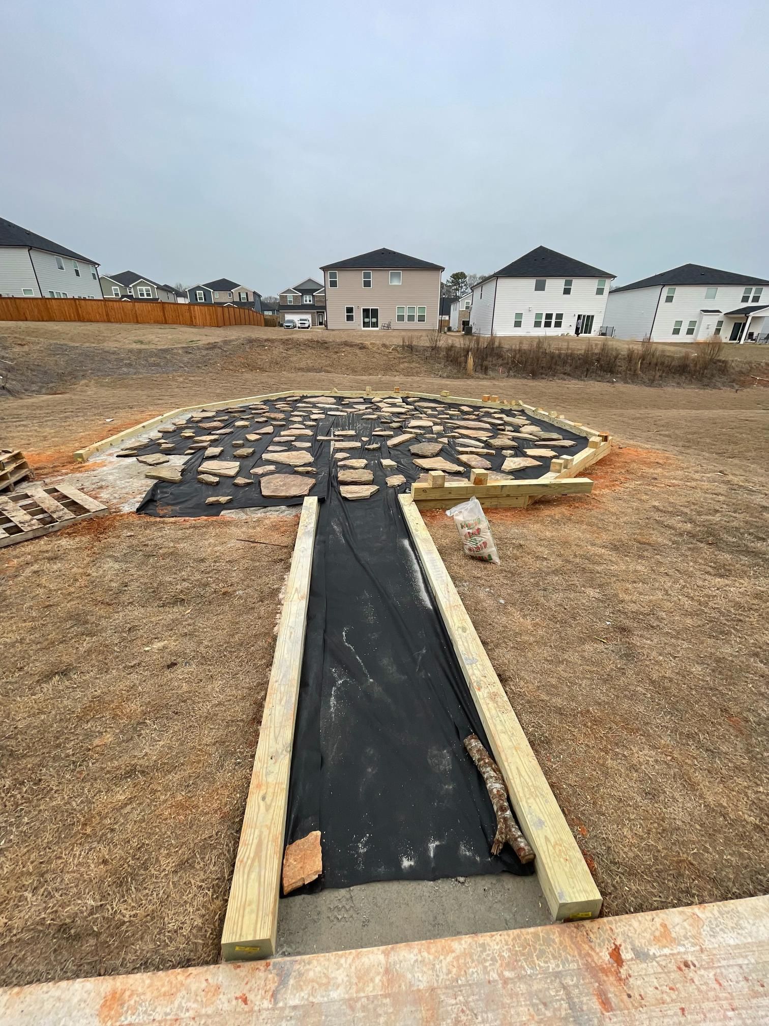 A wooden walkway going through a field with houses in the background.