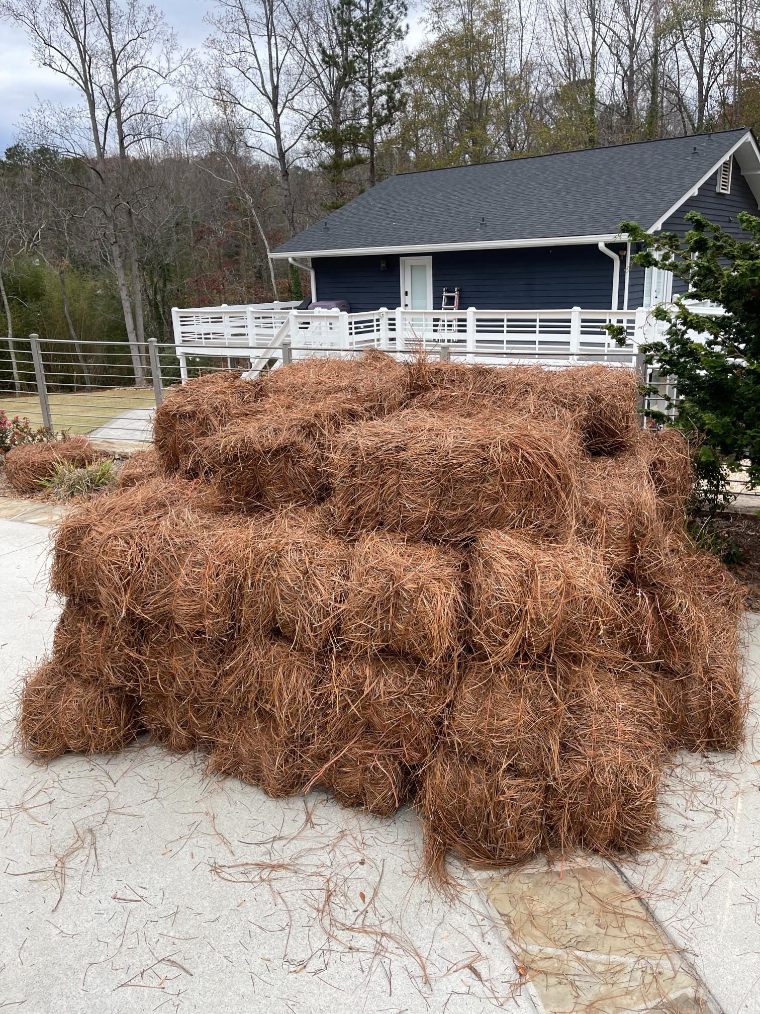 A pile of hay bales is sitting in front of a house.