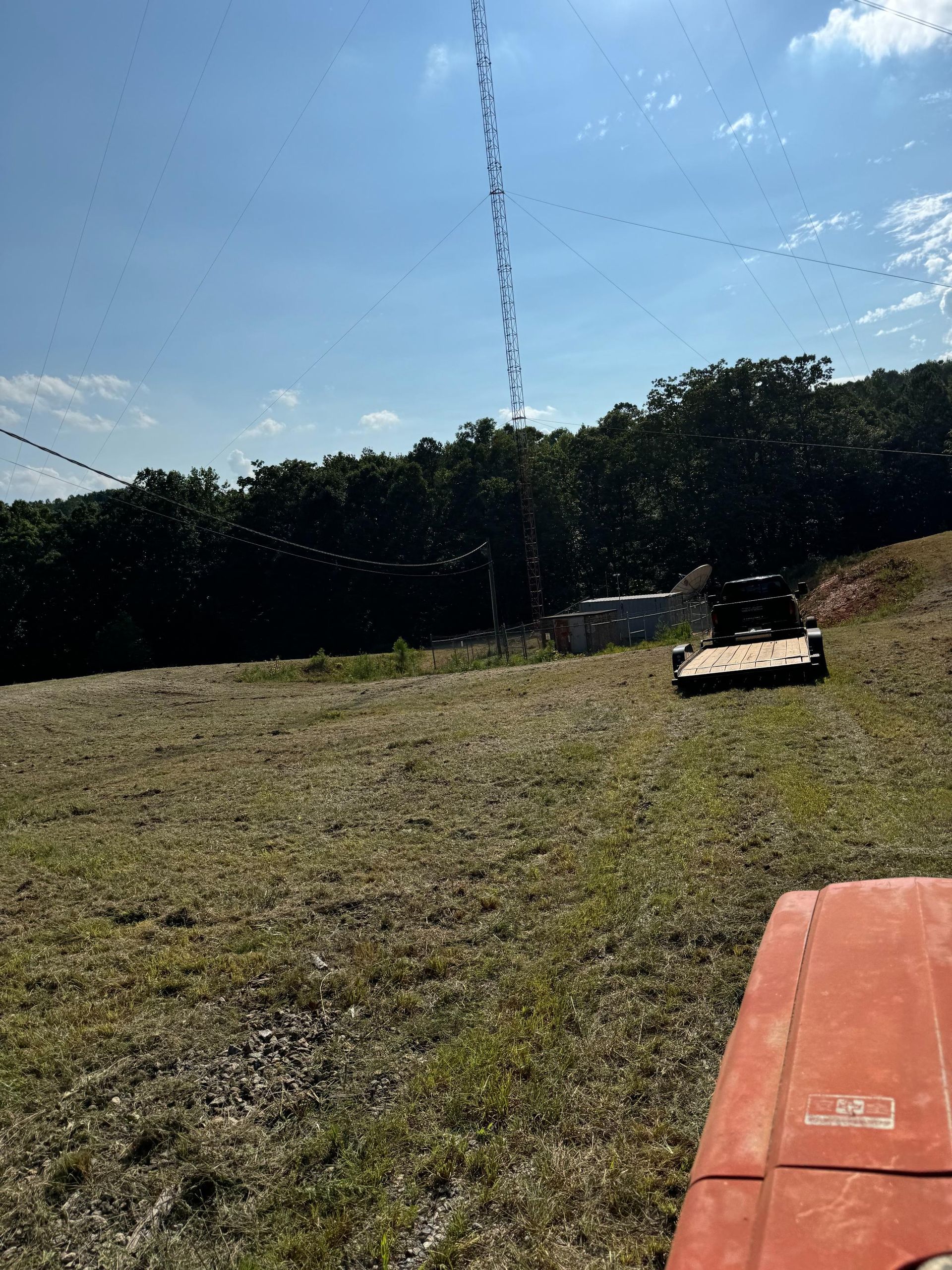 A tractor is cutting grass in a field with a tower in the background.