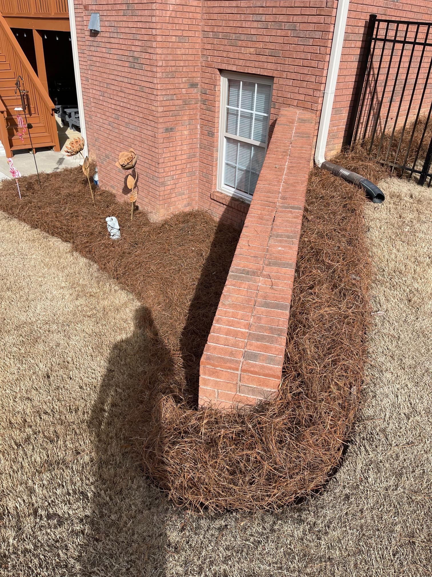 A brick wall is surrounded by mulch in front of a brick house.